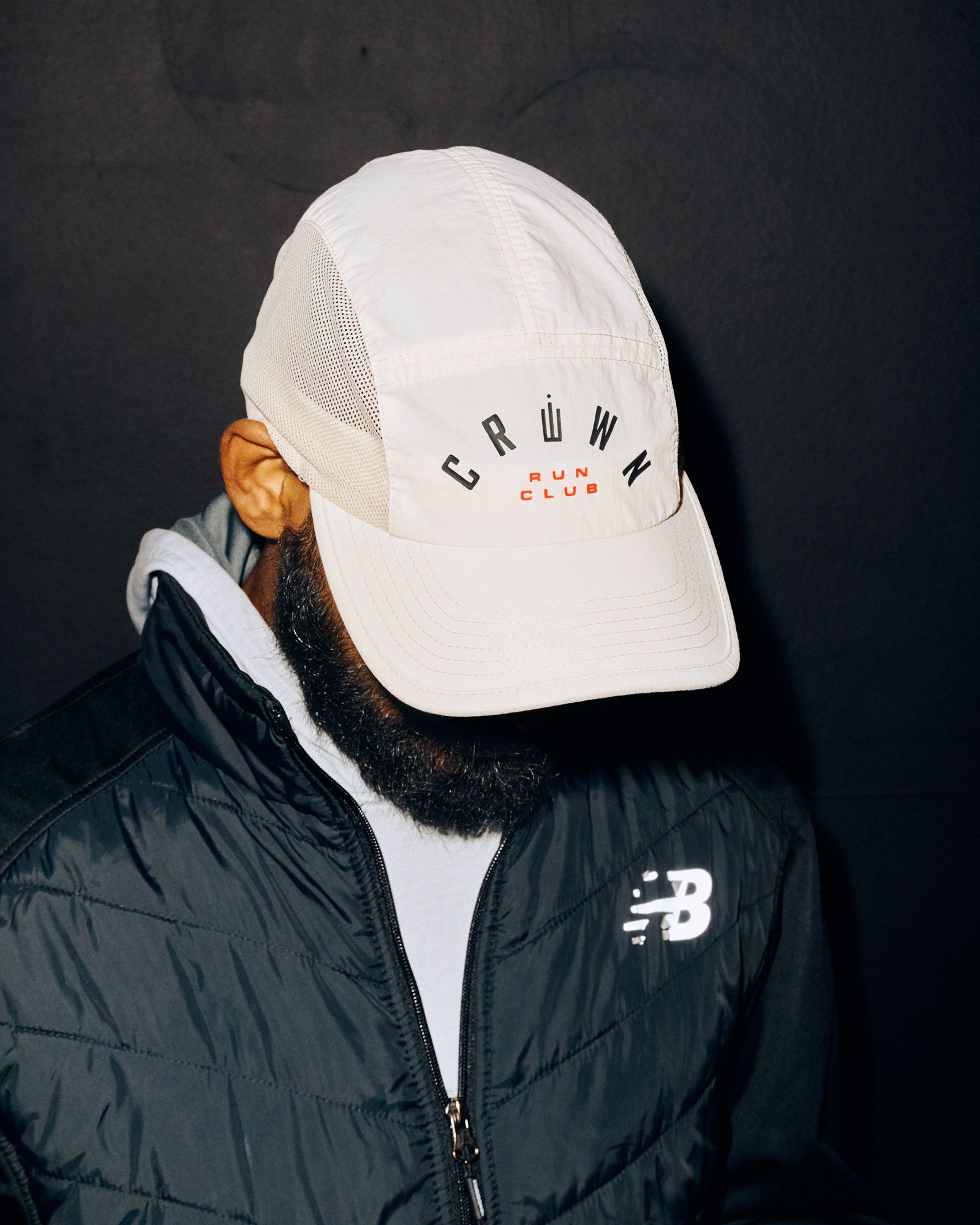 Ένα άτομο σε ένα μαύρο windbreaker της New Balance κλίνει το κεφάλι του πάνω από το πρόσωπό τους για να αναδείξει το λευκό στέμμα υψηλό τρέξιμο ...