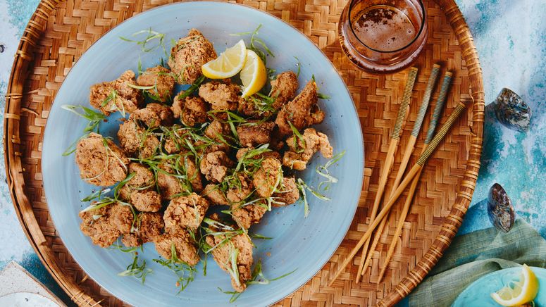 Mochiko Fried Chicken σε μια μπλε πλάκα πάνω από ένα υφαντό δίσκο με ξυλάκια και λεμόνι σφήνες.